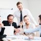 Welcome on board! Group of confident business people in formalwear sitting at the table together and smiling while two men handshaking